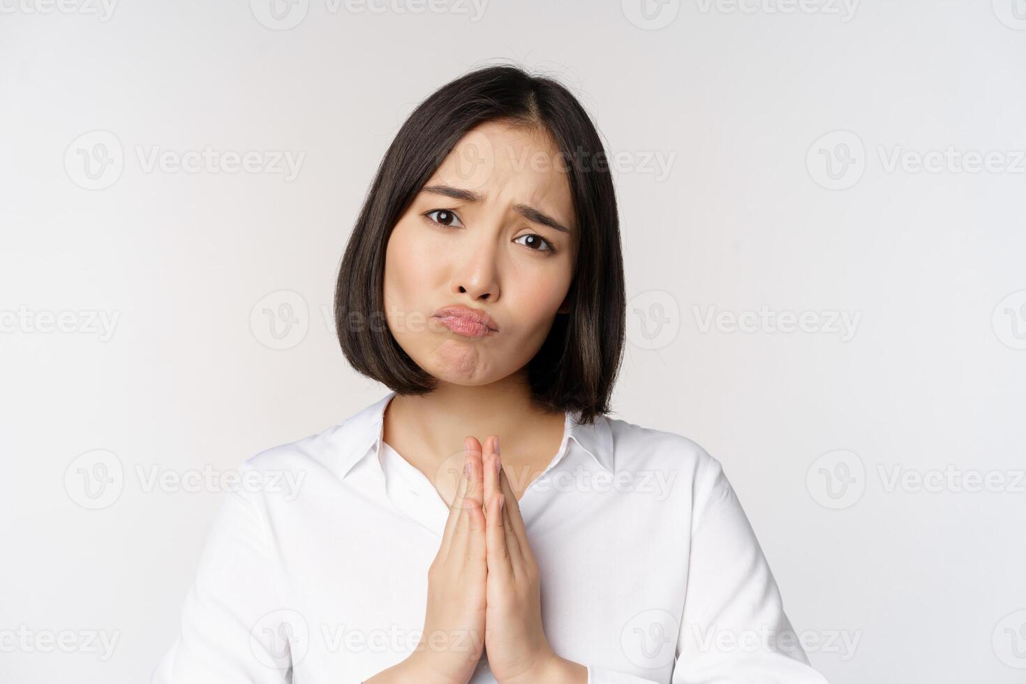 Close up portrait of asian woman begging, asking for smth, say please with coy sad face, need help, standing over white background photo