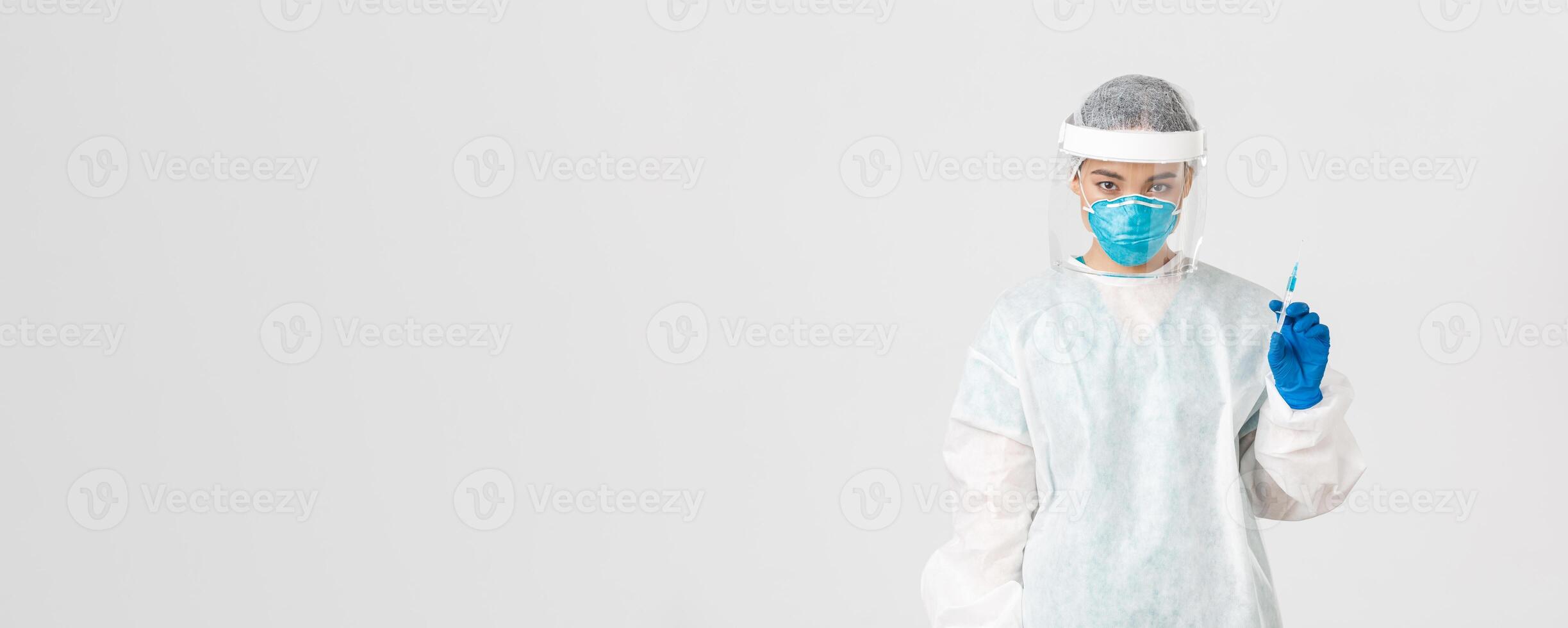 Covid-19, coronavirus disease, healthcare workers concept. Serious-looking confident asian female doctor in medical respirator and personal protective equipment, holding syringe with vaccine photo