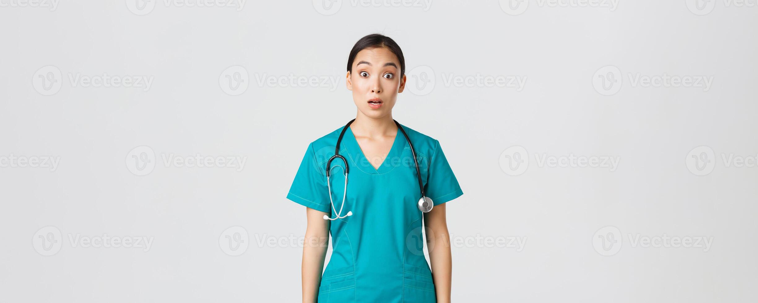 Covid-19, healthcare workers, pandemic concept. Impressed and surprised asian nurse in scrubs drop jaw and stare at camera speechless, looking amazed over white background photo