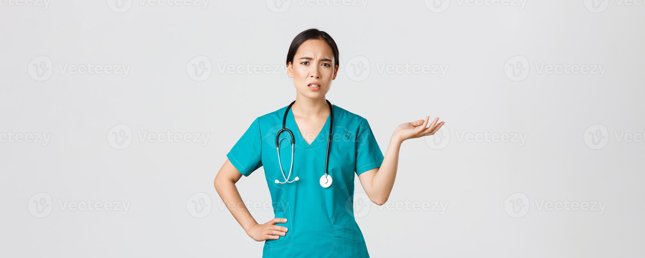 COVID-19, cuidado de la salud trabajadores, pandemia concepto. frustrado y irritado asiático hembra doctor, enfermero en matorrales aumento uno mano y mirando cuestionado y enfadado, quejumbroso alguna cosa foto