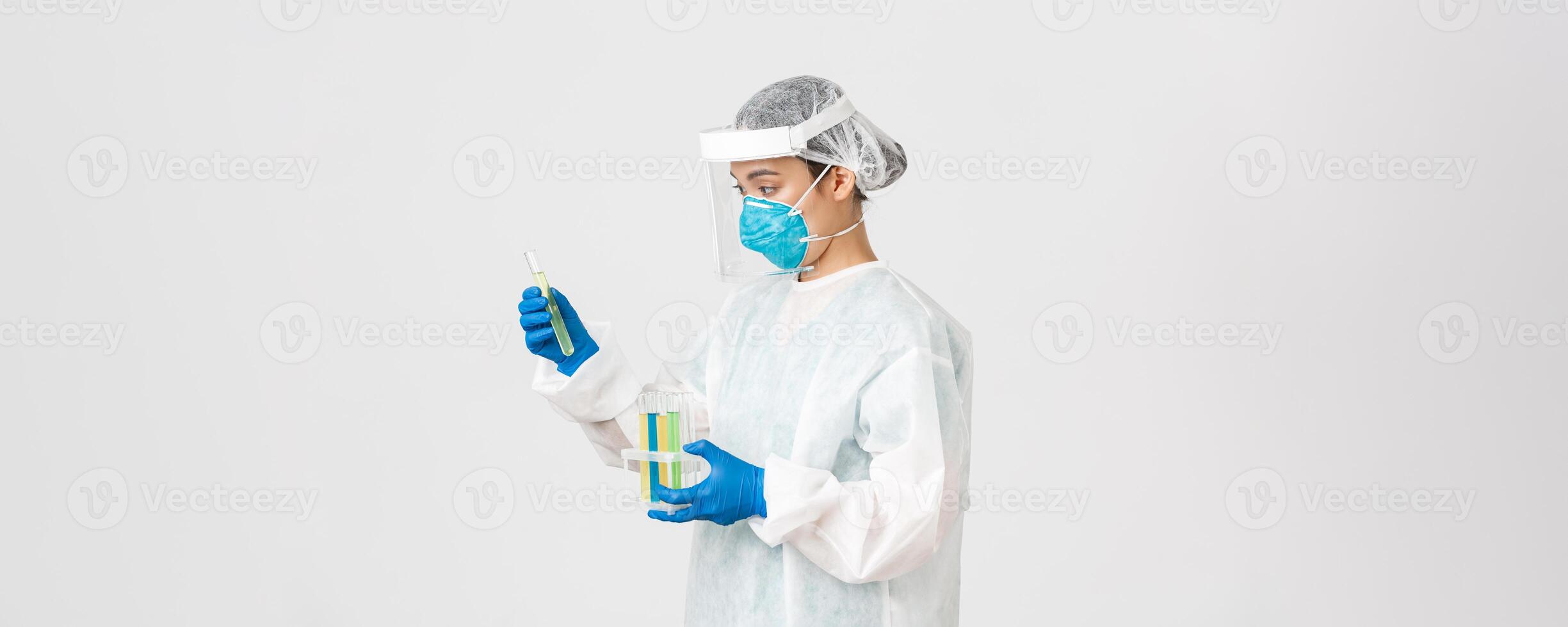 Covid-19, coronavirus disease, healthcare workers concept. Side view of careful serious asian female doctor, tech lab employee in personal protective equipment holding test-tube probes of vaccines photo