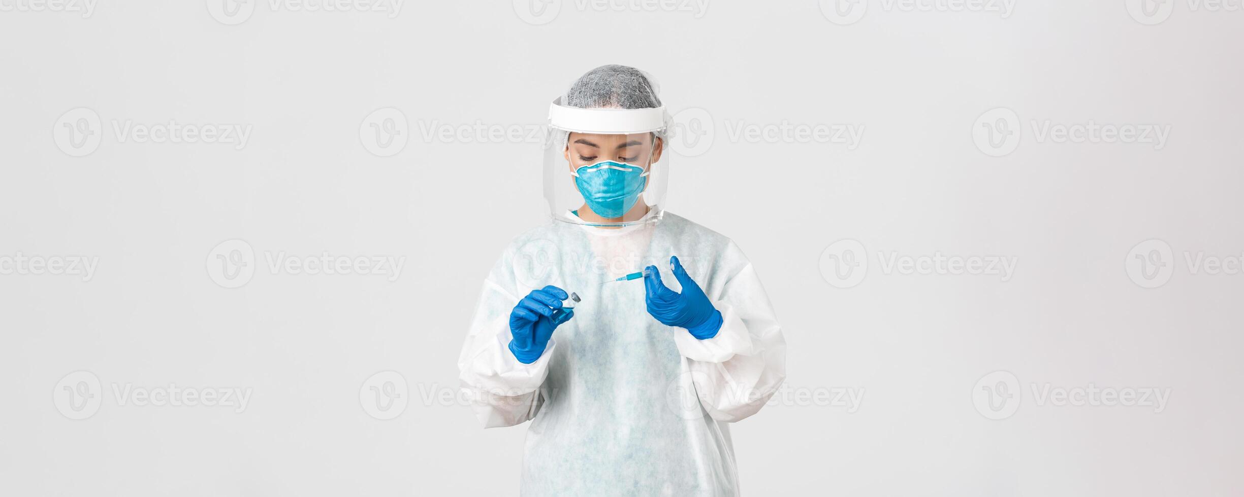 Covid-19, coronavirus disease, healthcare workers concept. Serious-looking female physician, asian doctor in personal protective equipment insert syringe in ampoule with vaccine, white background photo