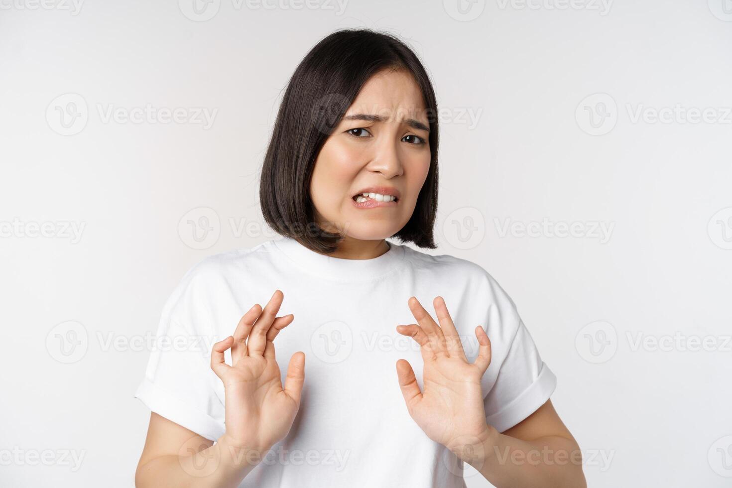 Disgusted asian woman rejecting smth, grimacing from dislike and aversion, stare with cringe, refusing offer, standing over white background photo