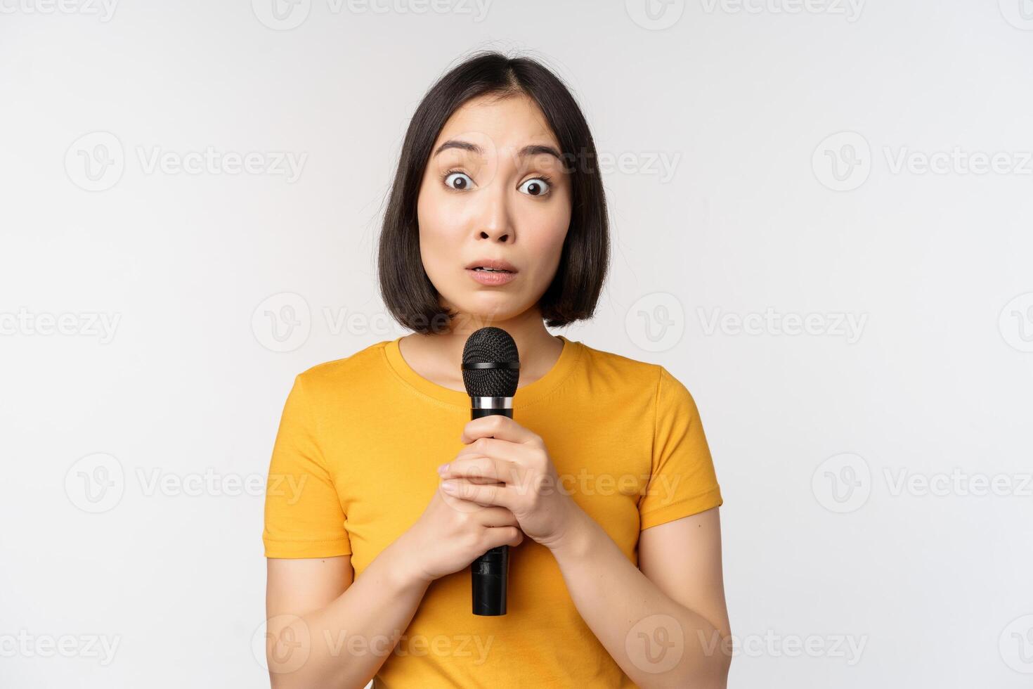 Modest asian girl holding microphone, scared talking in public, standing against white background photo