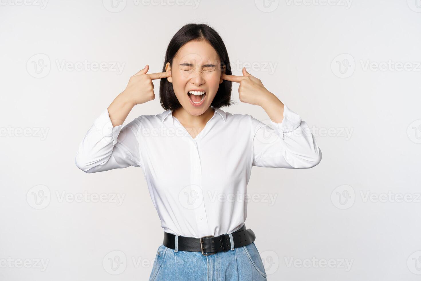 Annoyed asian woman feeling discomfort from loud annoying noise, close ears and eyes, standing over white background photo