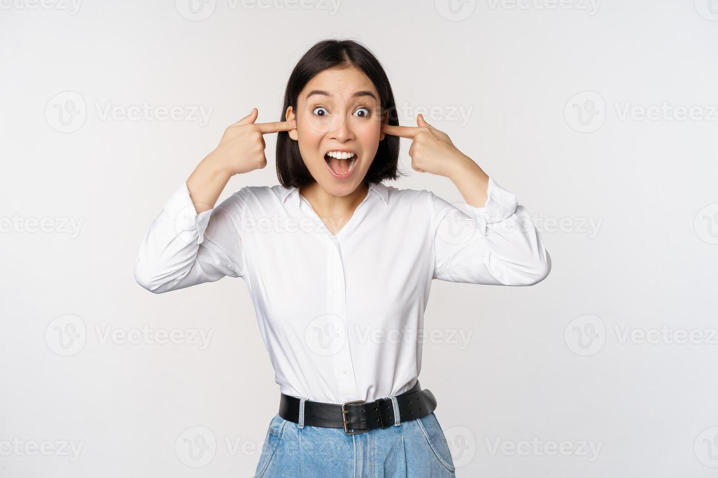 Young annoyed asian girl close ears and screaming, fed up with loud noise, terrible music, standing over white background photo