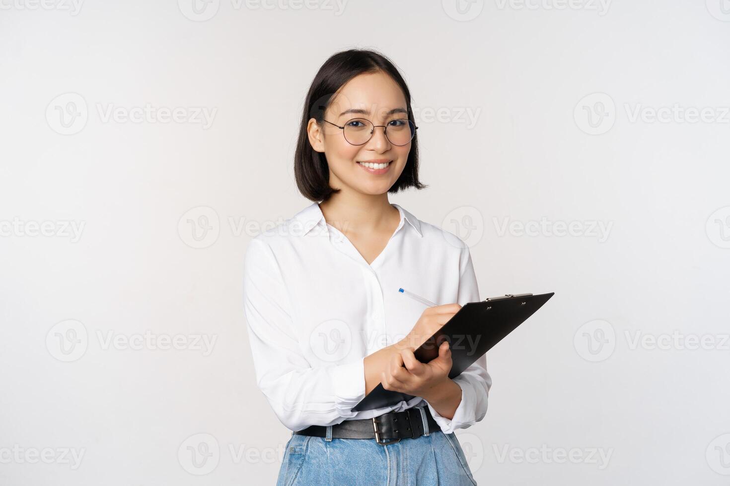 Image of smiling korean office lady, company employee writing down on clipboard, taking notes, standing over white background photo