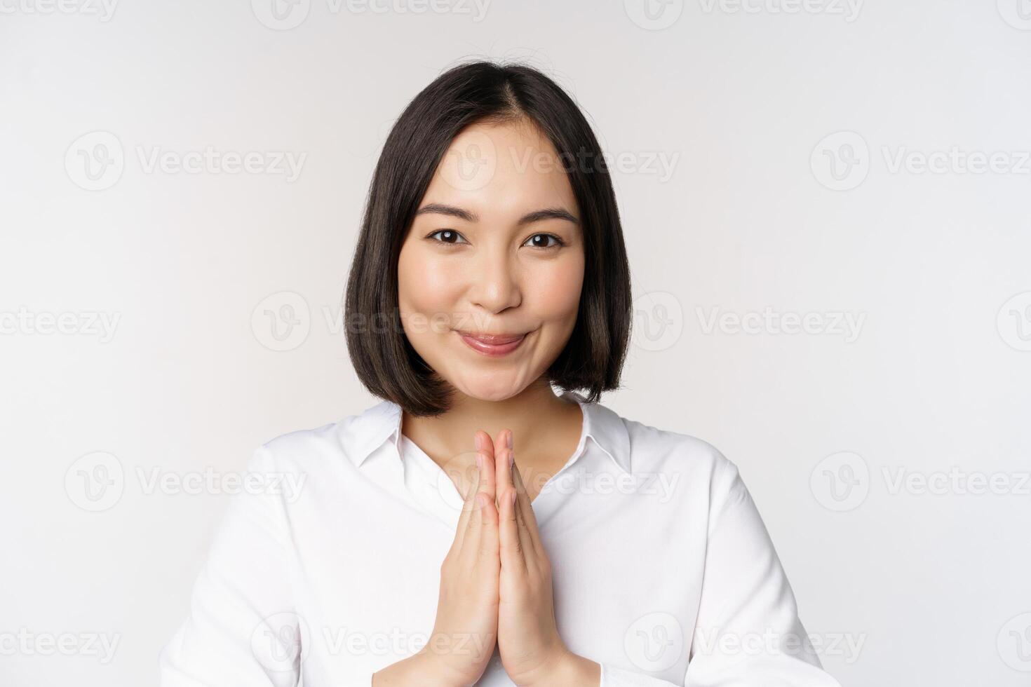 Close up portrait of young japanese woman showing namaste, thank you arigatou gesture, standing over white background photo