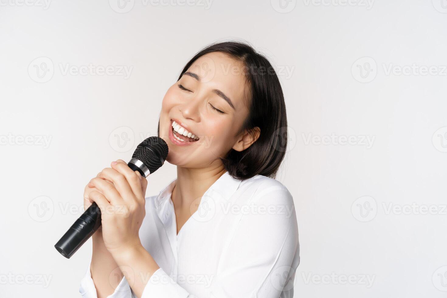 cerca arriba retrato de asiático mujer canto en micrófono a karaoke, en pie terminado blanco antecedentes foto