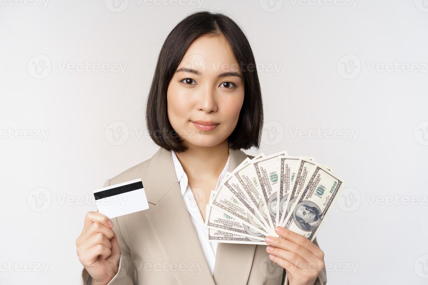 Close up of asian businesswoman, office lady showing credit card and money dollars, standing in suit over white background photo