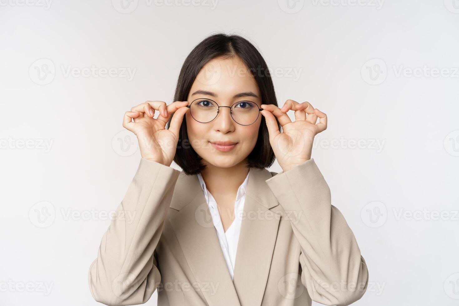 Smiling asian businesswoman trying new glasses, wearing eyewear, standing in suit over white background photo