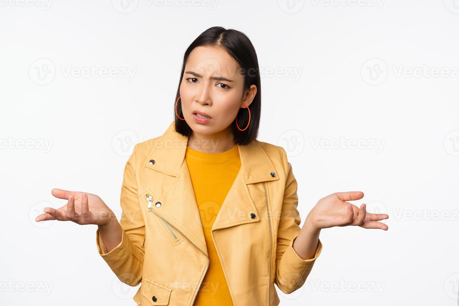 Image of confused young asian woman shrugging shoulders, looking puzzled and clueless at camera, cant understand, standing against white background photo