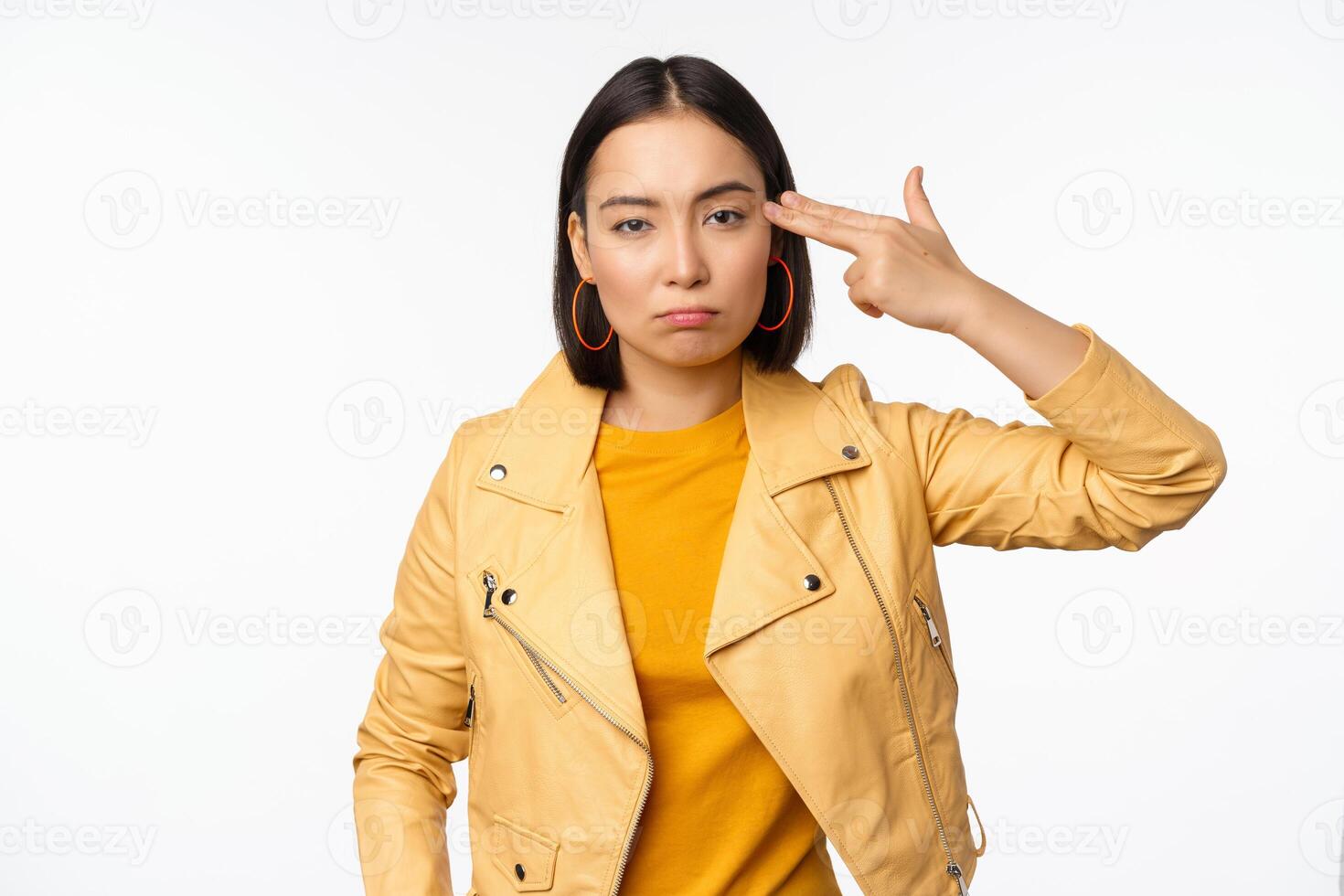 Image of annoyed and tired asian girl, making hand-gun gesture, fingers near temple, looking bored and distressed, standing against white background photo