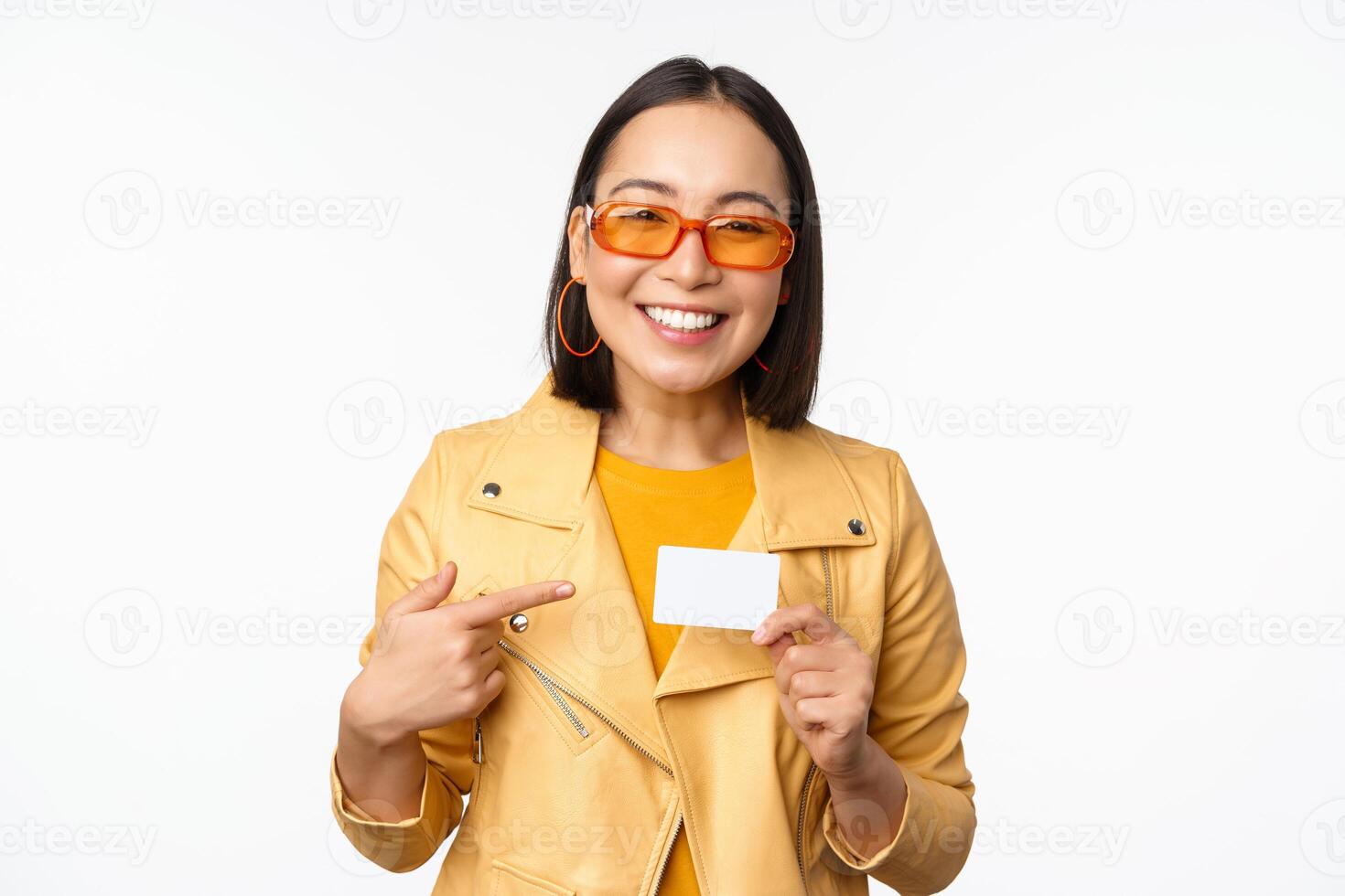 Portrait of beautiful modern asian girl in sunglasses, smiling happy, showing credit card, standing over white background photo