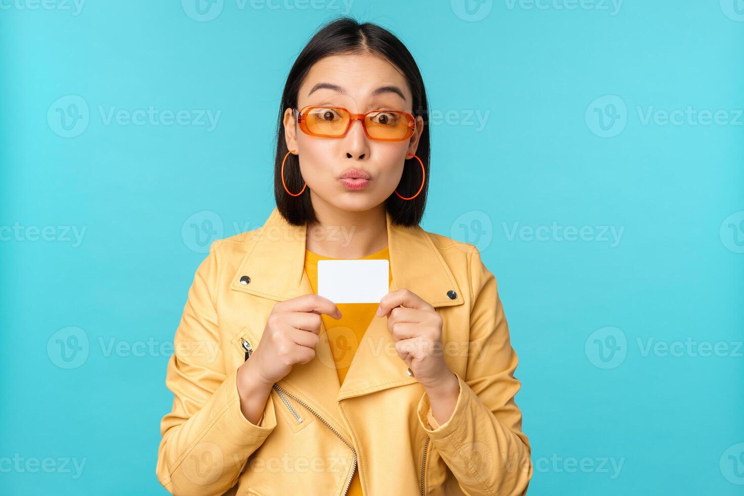 Young beautiful asian woman showing credit card, smiling, choosing bank, standing over blue background photo