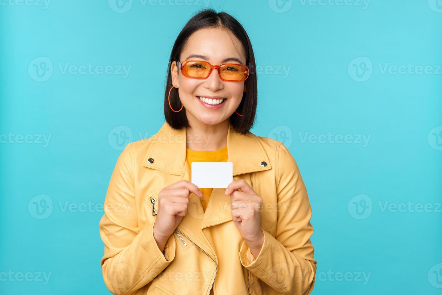 Young beautiful asian woman showing credit card, smiling, choosing bank, standing over blue background photo