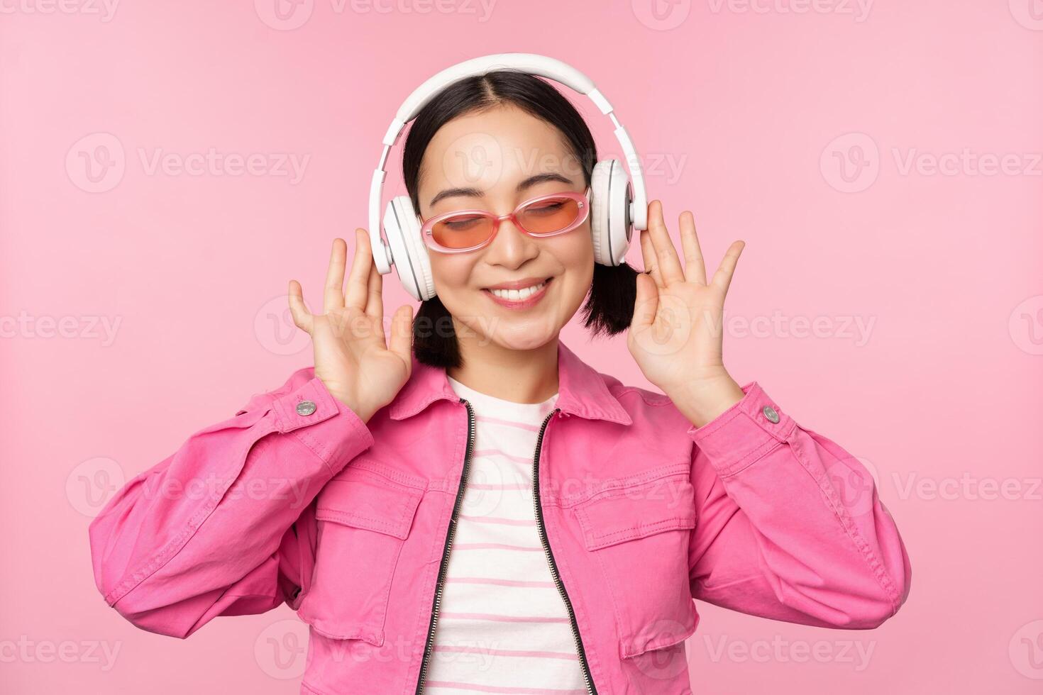 bailando elegante asiático niña escuchando música en auriculares, posando en contra rosado antecedentes foto