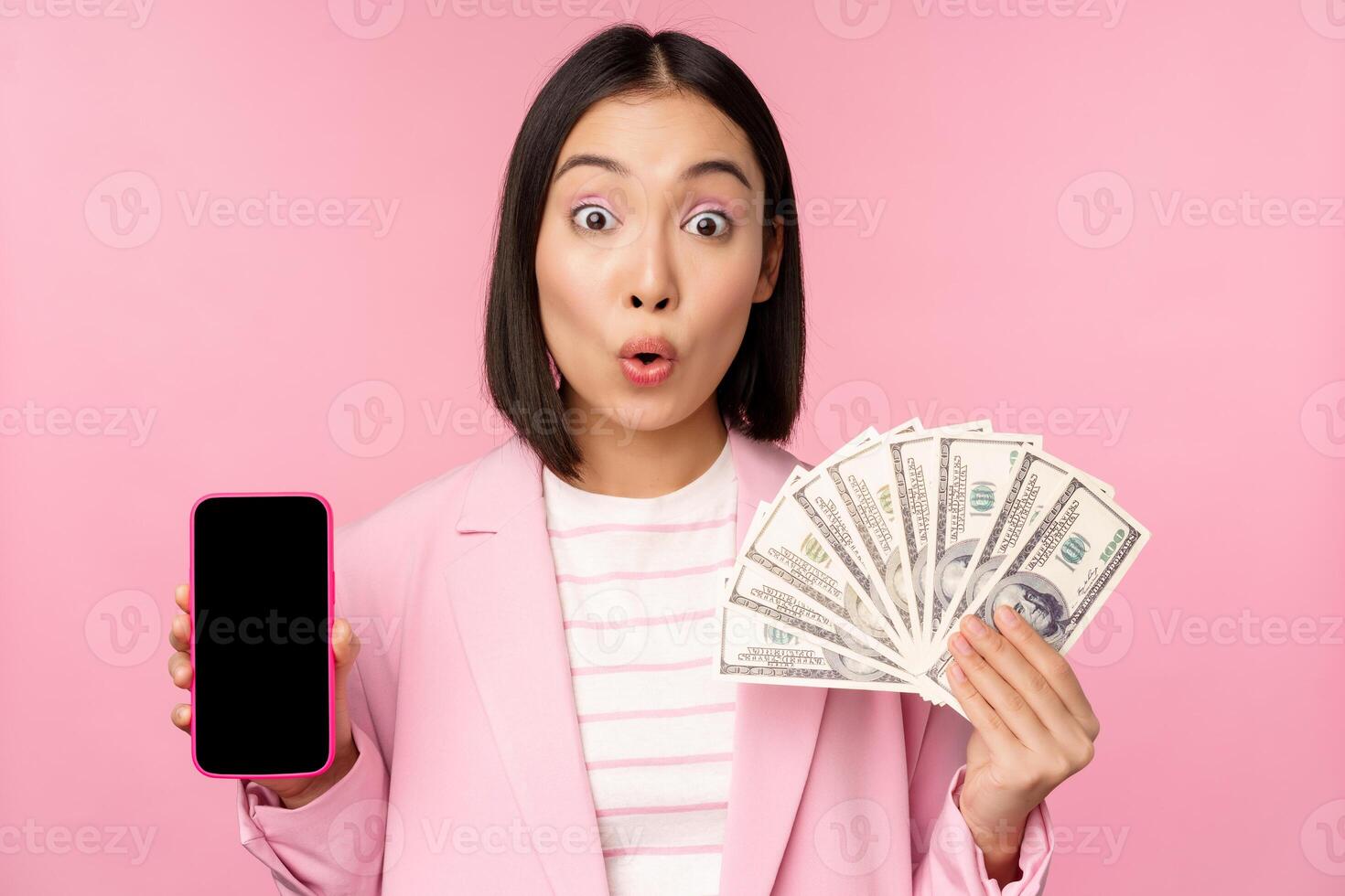 Image of korean successful corporate woman showing money, dollars and smartphone app screen, interface of mobile phone application, concept of investment and finance, pink background photo