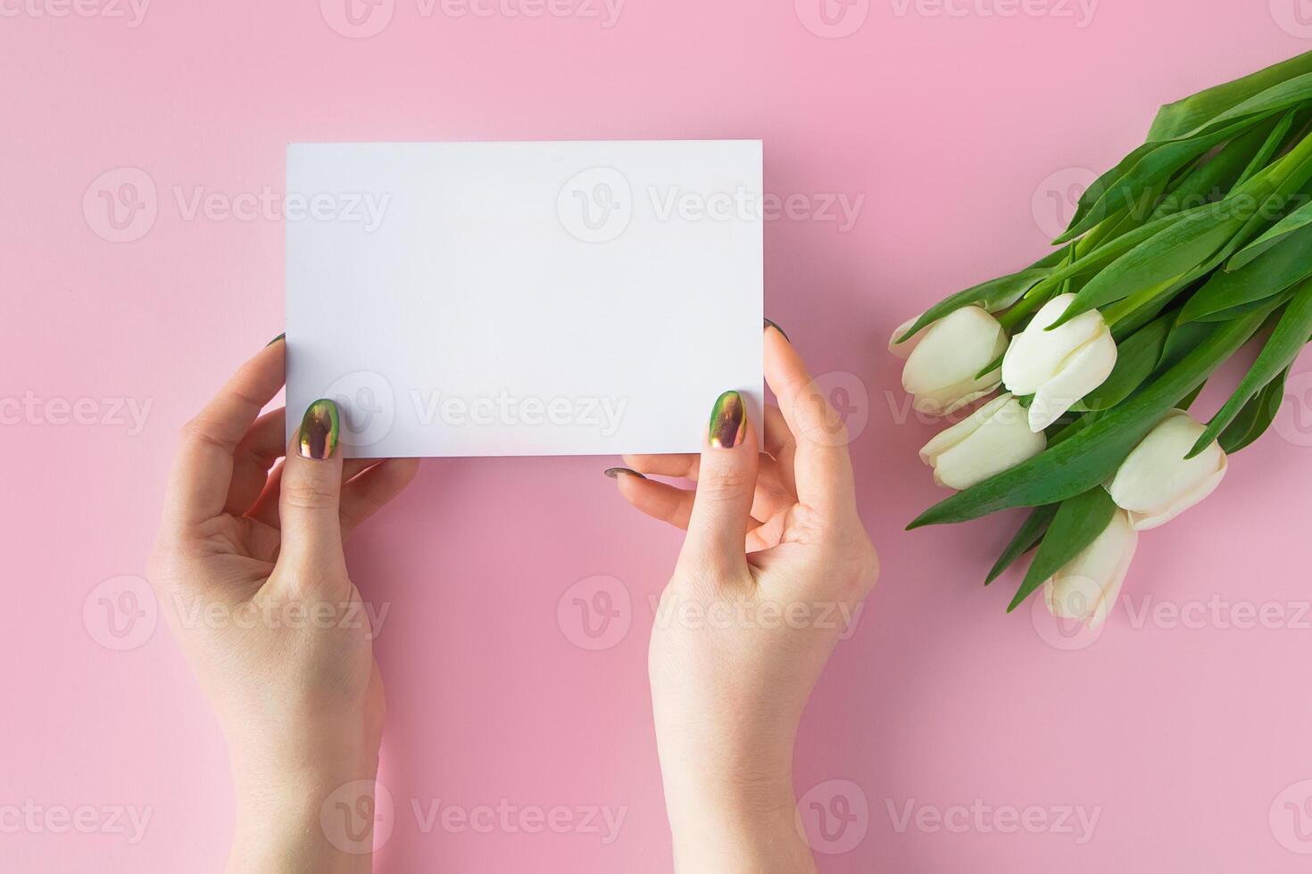 mujer sostiene saludo tarjeta en su manos. ramo de flores de Fresco tulipanes en rosado antecedentes. foto
