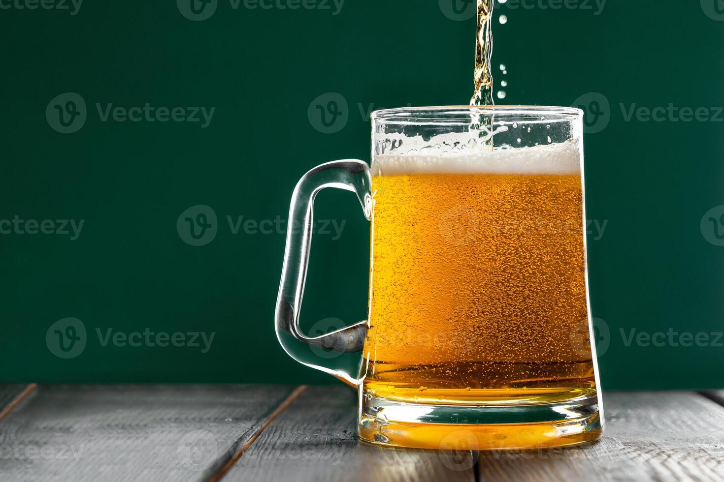 Beer is pouring into a mug on a green background. Celebrating St. Patrick's Day. Traditional Irish drink. photo