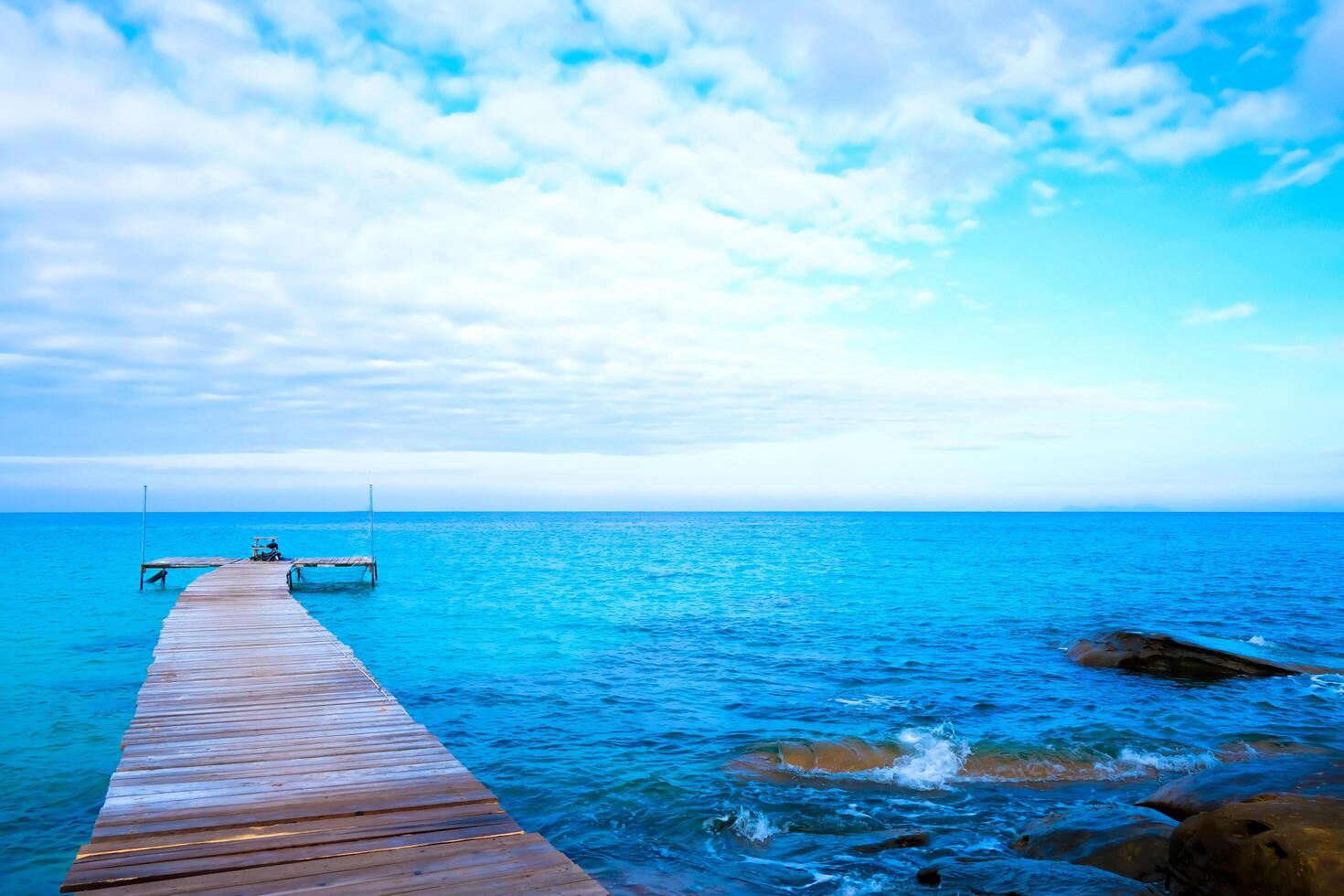 The wooden bridge stretches into the sea.With mountain clouds and sky. photo