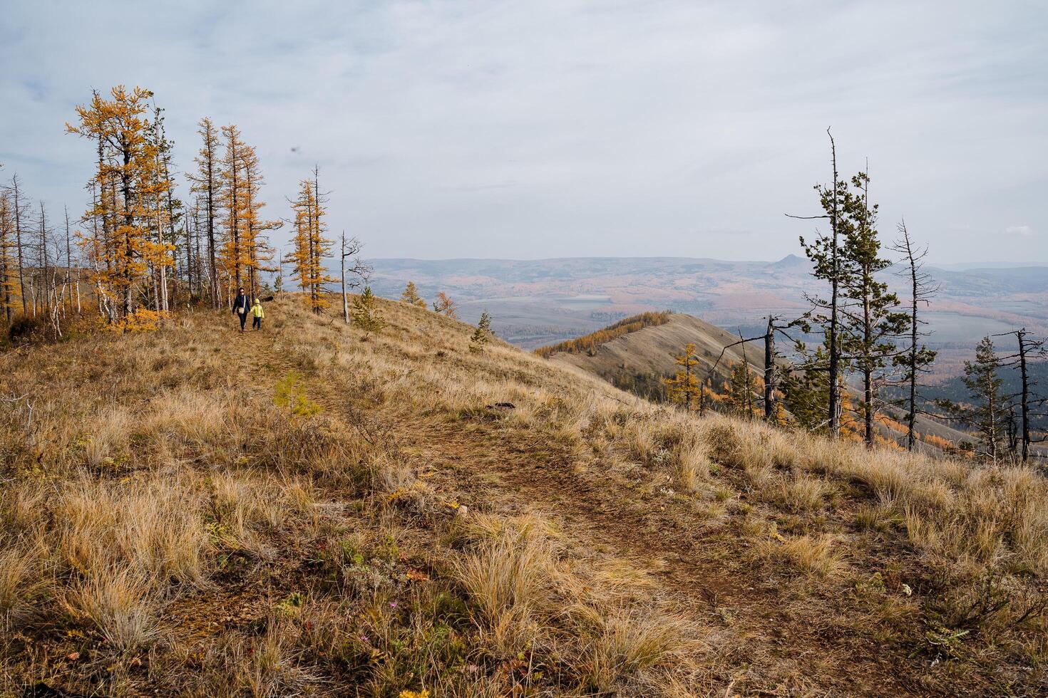 Panoramic view from the mountains to the surroundings, autumn landscape and golden forest, dark clouds overhead. A group of tourists walks to the top of the mountain. photo
