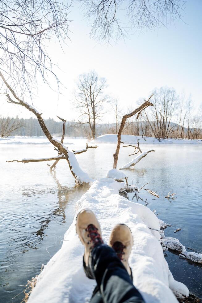 A shot of the feet of a man lying comfortably on a log in the middle of a winter ice-free lake. Outdoor activities in winter, winter entertainment photo