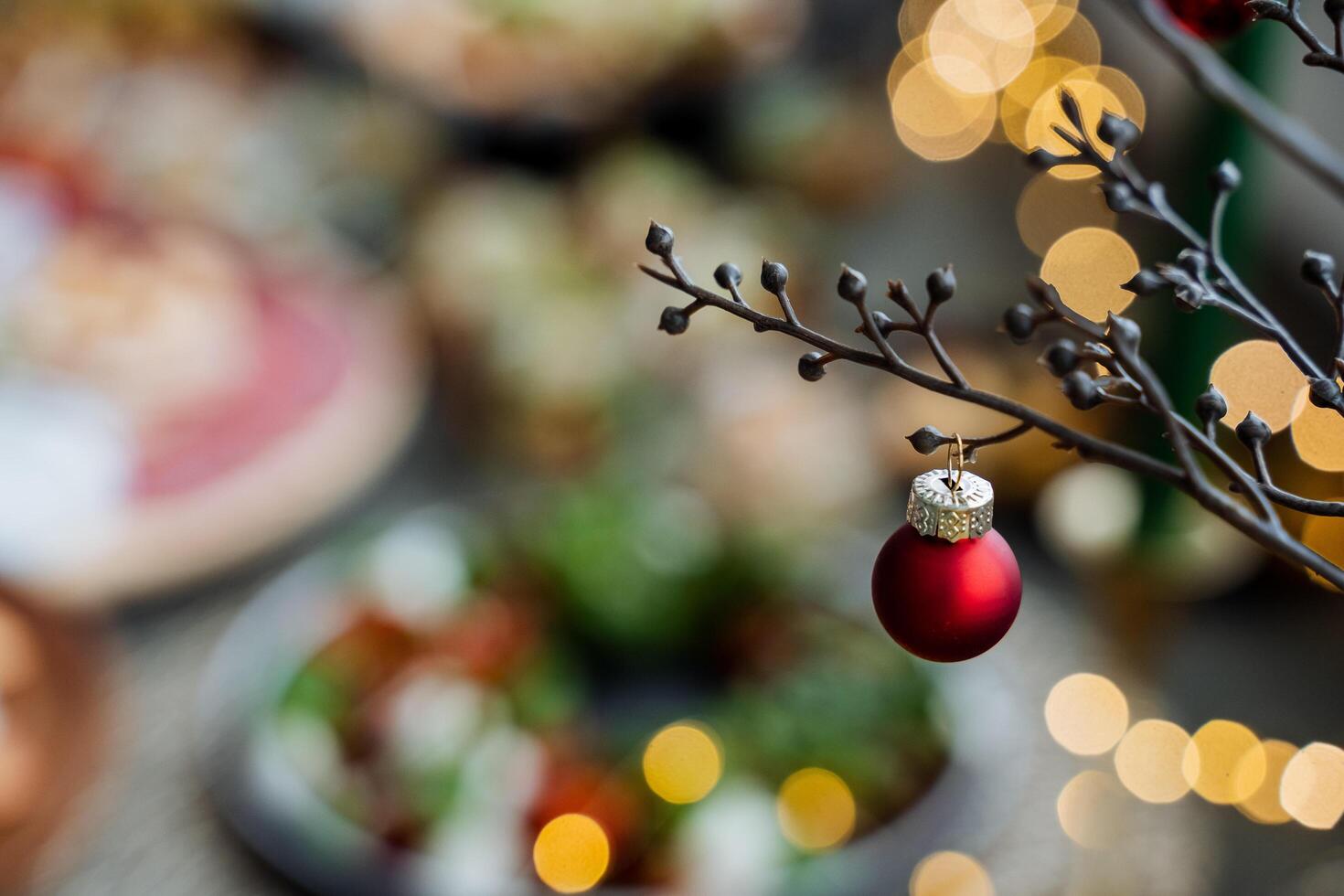 A red Christmas tree toy hangs on a leak against the background of lights. Decoration of the Christmas table. A red ball on a blurred background. New Year's mood photo