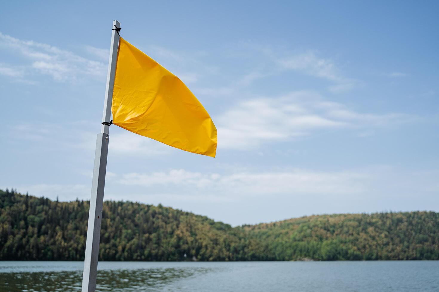 A bright yellow flag flies over the water. In the background are green mountains. photo