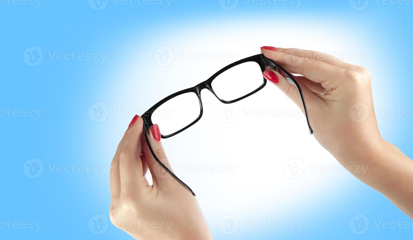 Female hand holding a black-framed glasses isolated on blue background photo