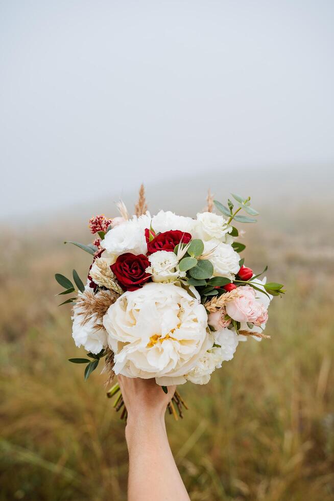 The bride with a thin and elegant hand holds a wedding bouquet of delicate white and red flowers photo