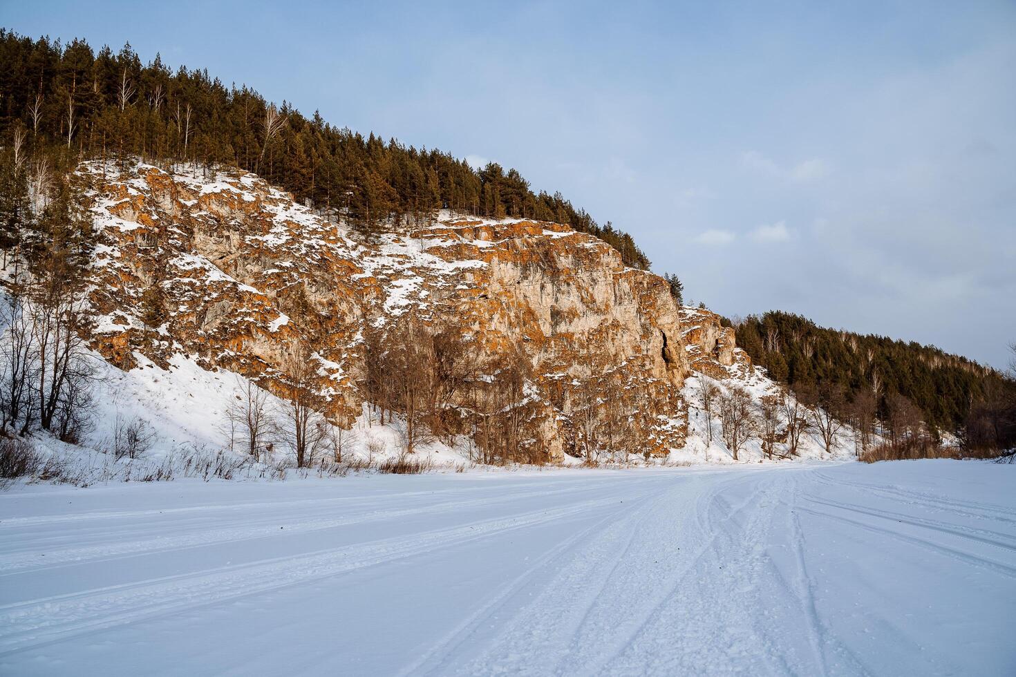 Winter landscape of a rock on the bank of the river. The rocky mountains of orange color are strewn with snow. Cold Russian winter. Ural Mountains photo