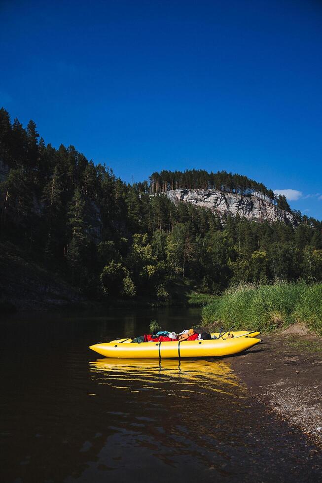 Bright yellow kayak without people on the shore near the mountains. There is no one next to the kayak. photo