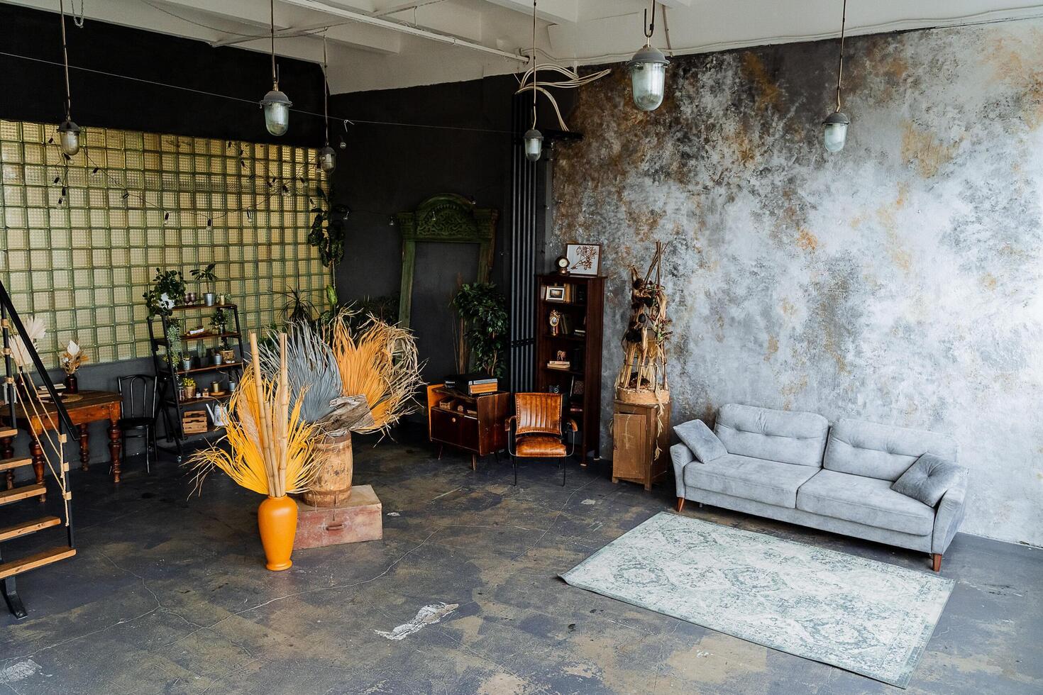 interior shot in the studio. loft studio.a lot of light, an unusual decorative wall, A bookcase full of books. a chic gray sofa, an orange vase with dry leaves, nearby stairs. Arrangement photo