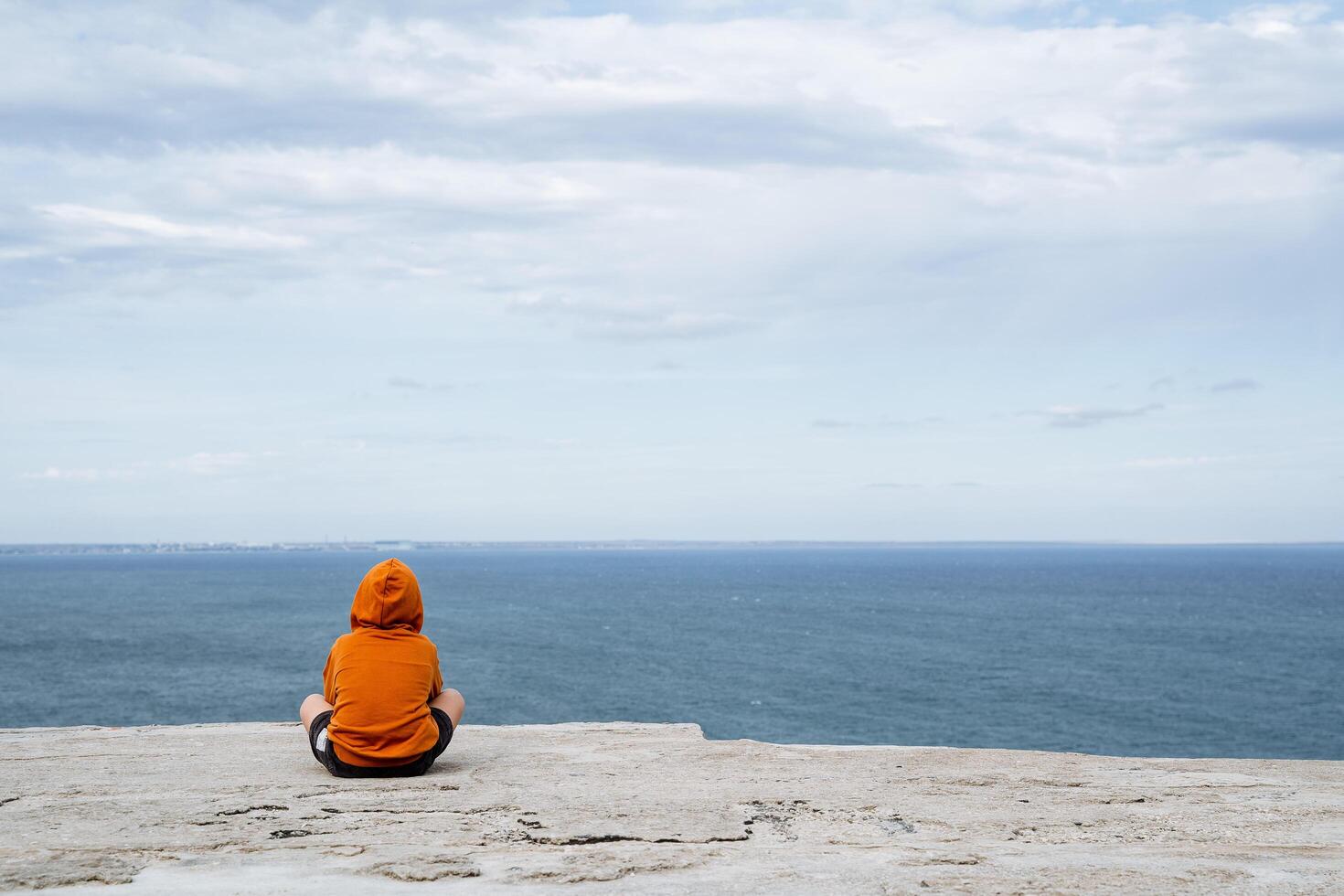 un hombre se sienta en el marco, frente a el mar. minimalista Disparo de hombre y el mar. brillante ropa, calma mar. hora solo. progulka por el mar foto