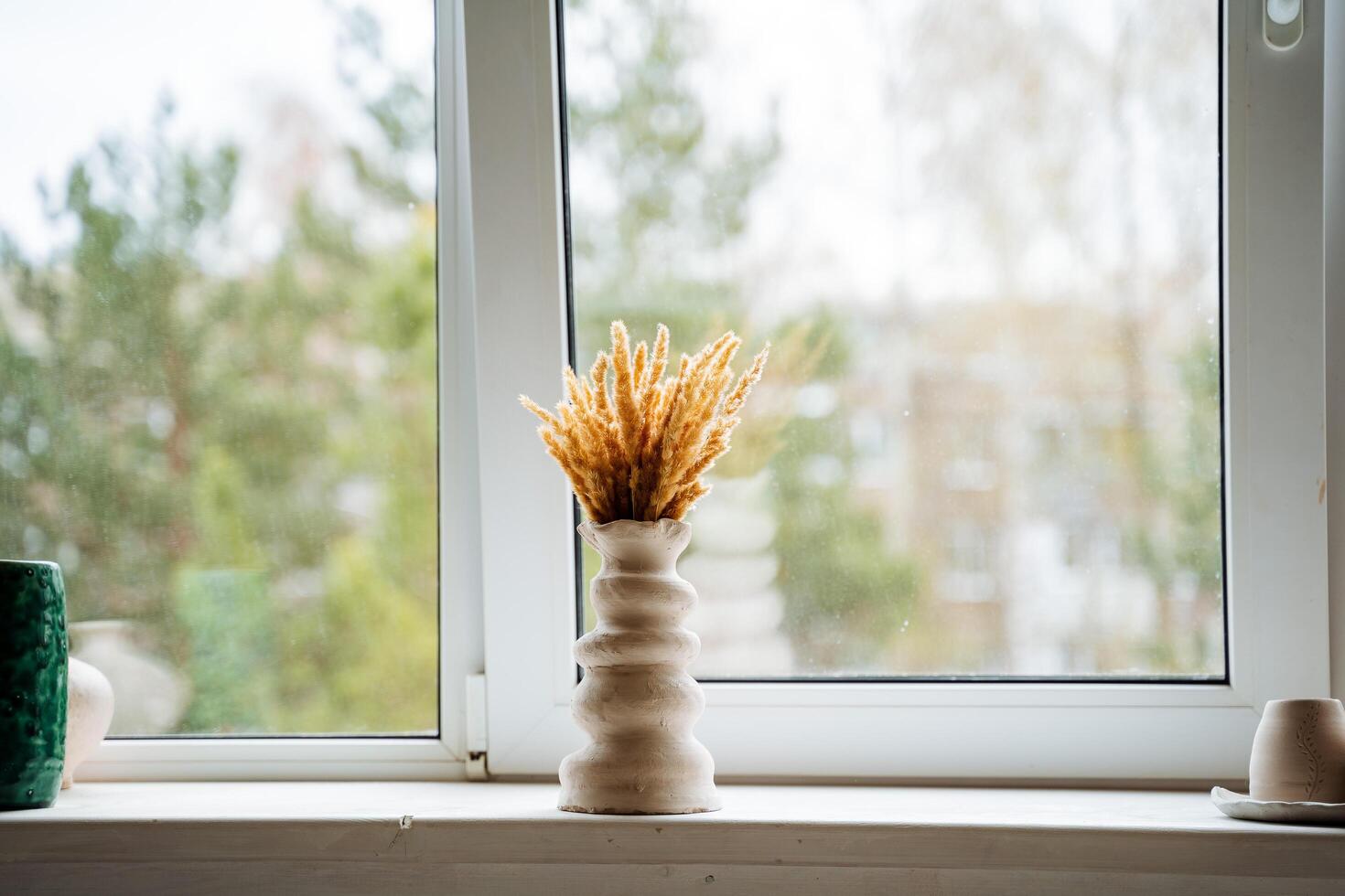 A vase of abstract shape stands in the middle of a light window sill in the workshop. Bouquet of yellow dried flowers in a vase. photo