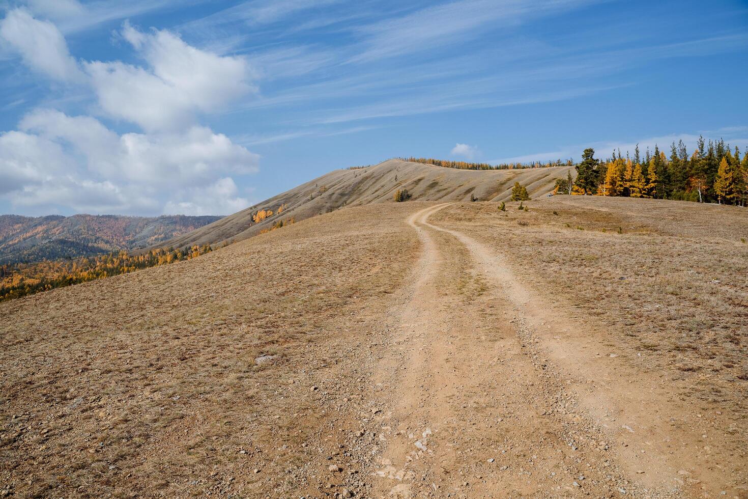 A long winding road goes through a mountain range. Sunny day, clear blue sky overhead, mountain landscape with autumn forest. photo