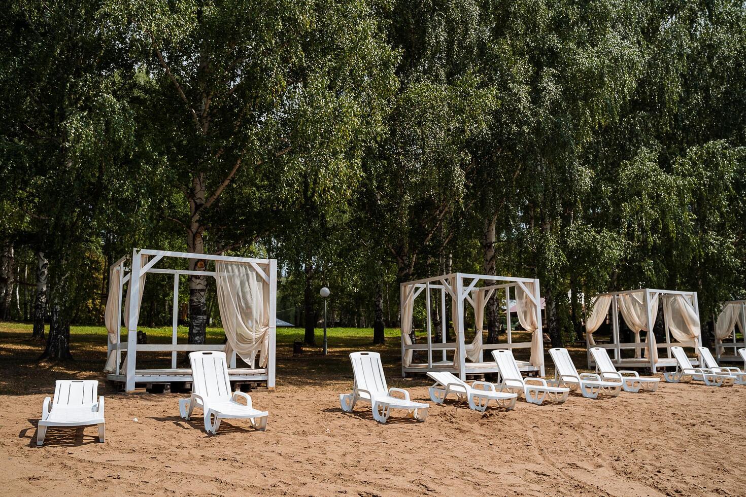 White sun loungers and tents for relaxing on the sandy empty beach. Rest by the water on a sunny summer day. photo