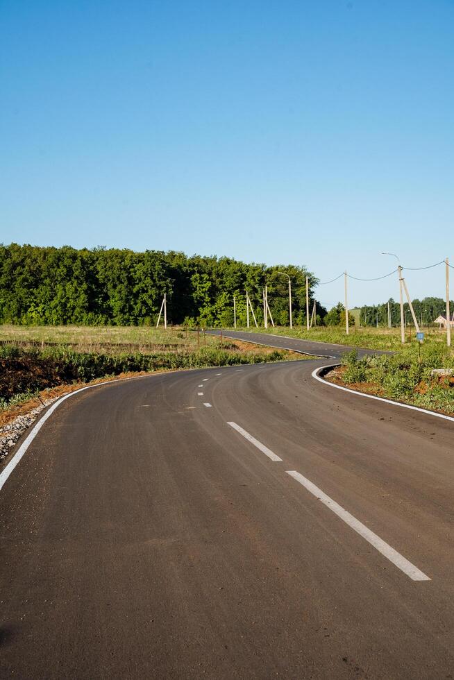 Motor road. An empty asphalt road with a bend between flower meadows in the countryside. A trip on a sunny day in summer photo