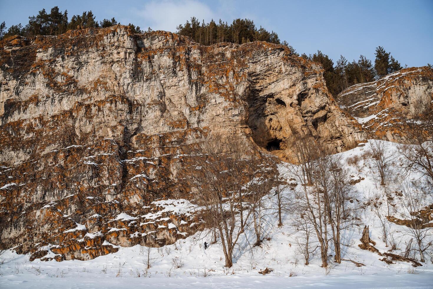 Winter landscape of a rock on the bank of the river. The rocky mountains of orange color are strewn with snow. Cold Russian winter. Ural Mountains photo