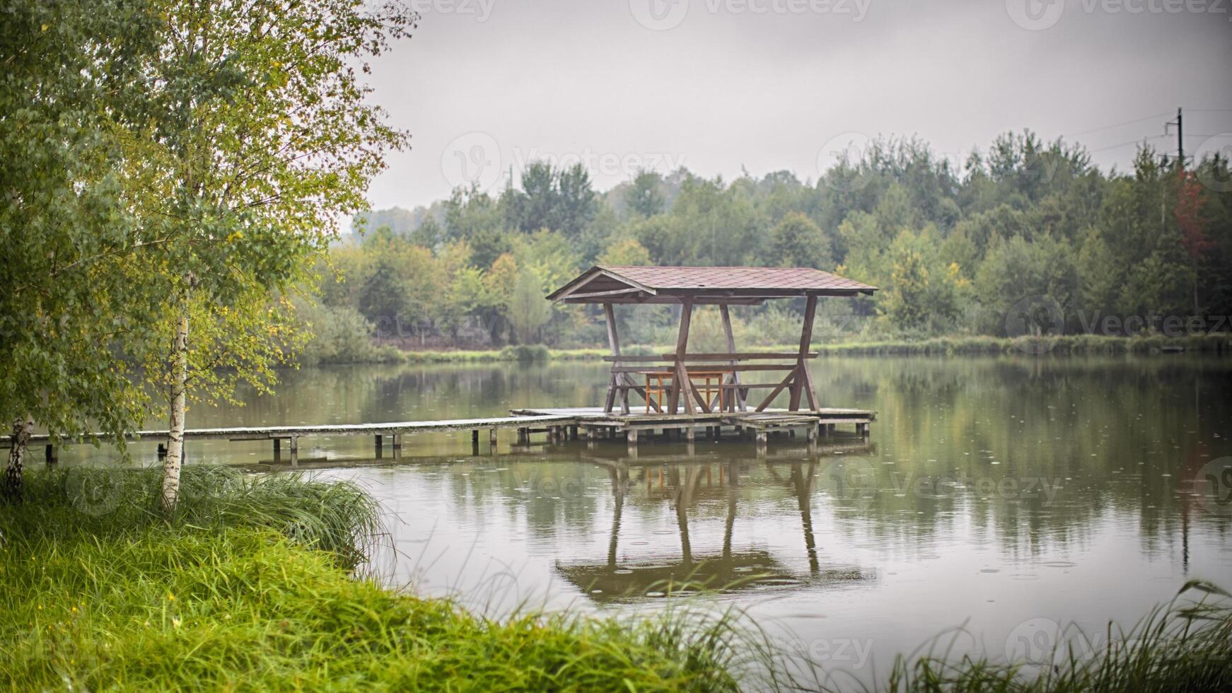 gazebo with chairs and a table stands on a wooden masonry in the middle of the lake photo