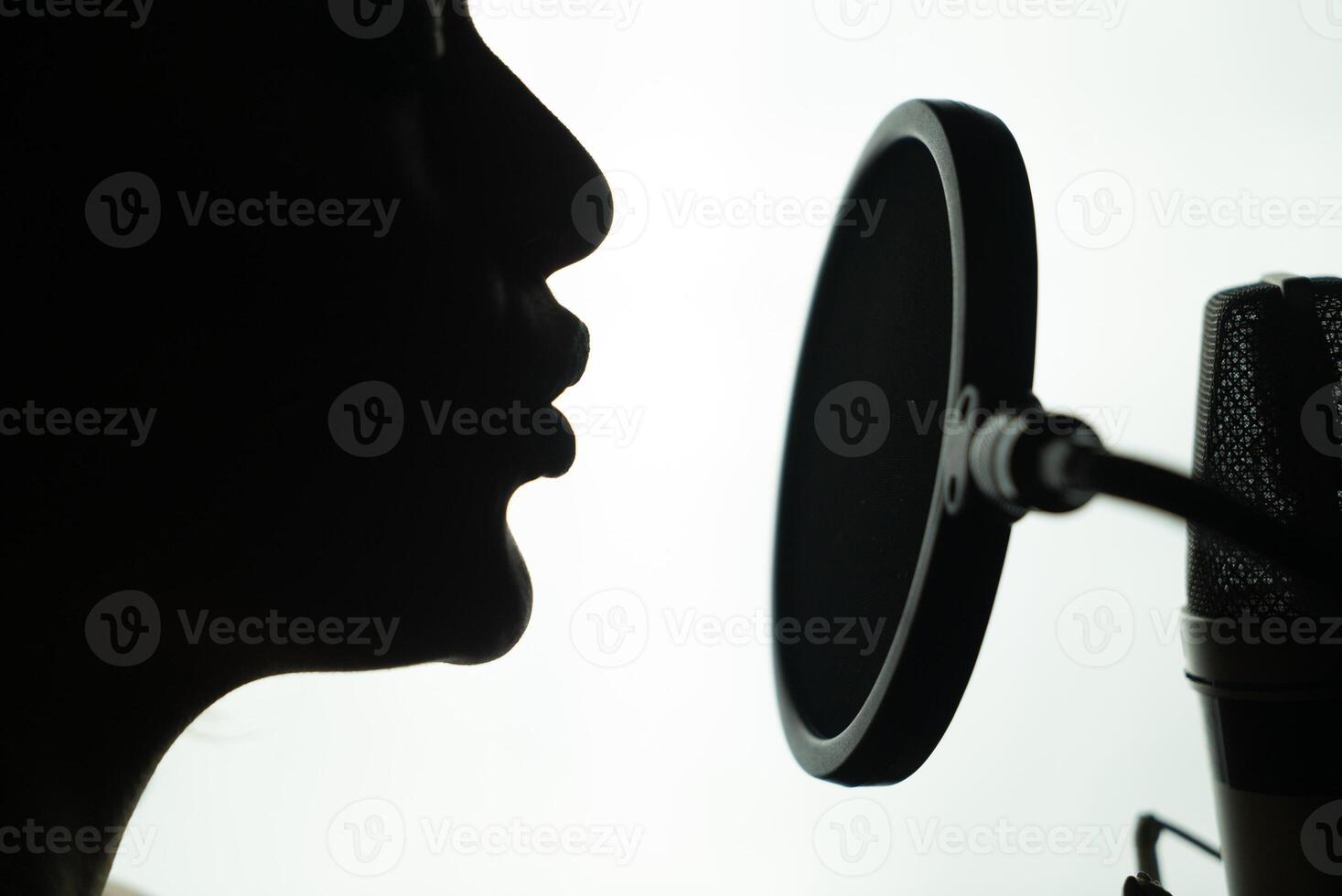 Black and white profile of a young woman singing at the round microphone. Close-up of female's face near the mic. photo