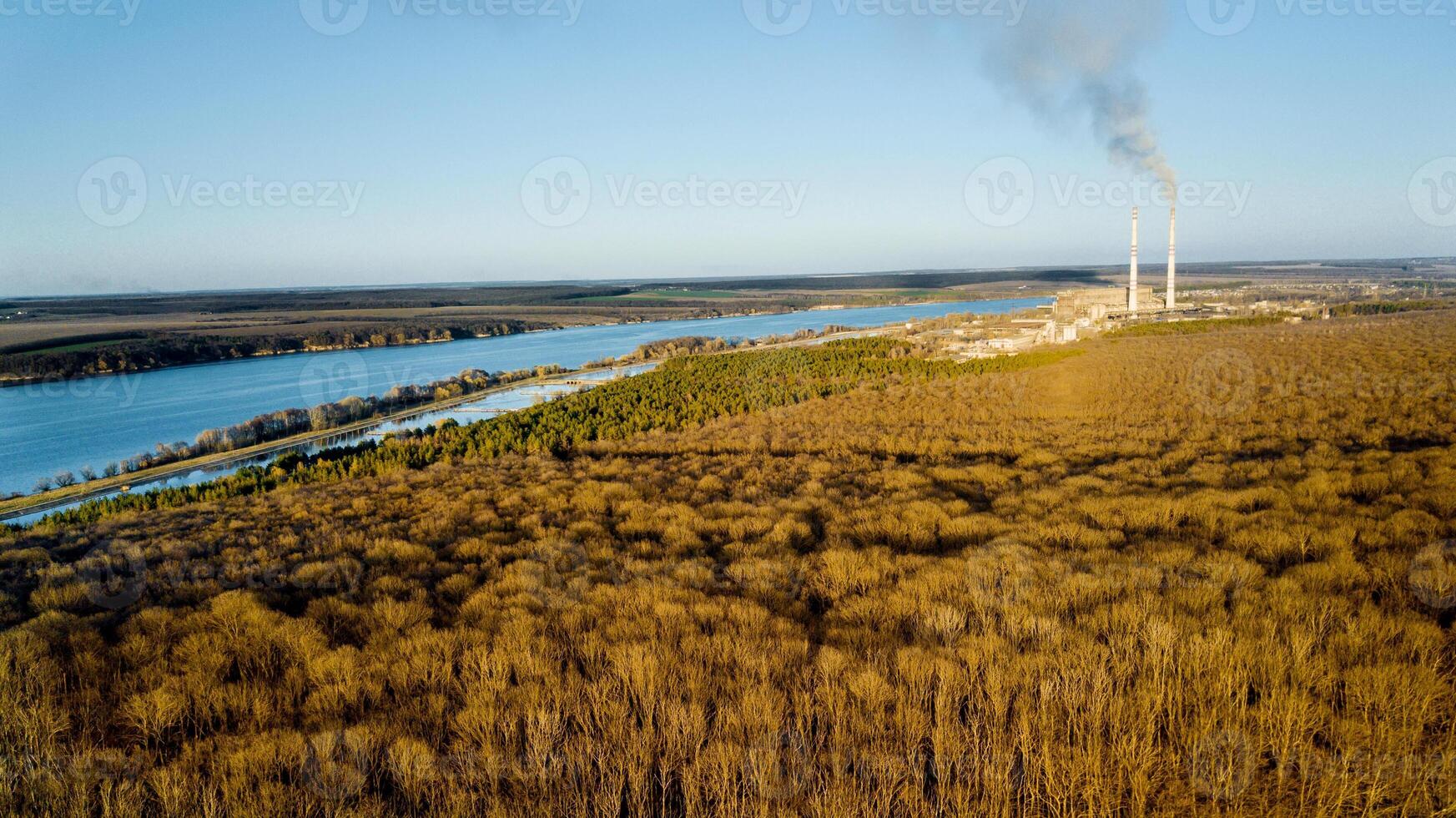 Aerial view of the forest in early spring, blue river and fields under the clear sky. Natural background and a factory with smoke which comes out from the pipes photo
