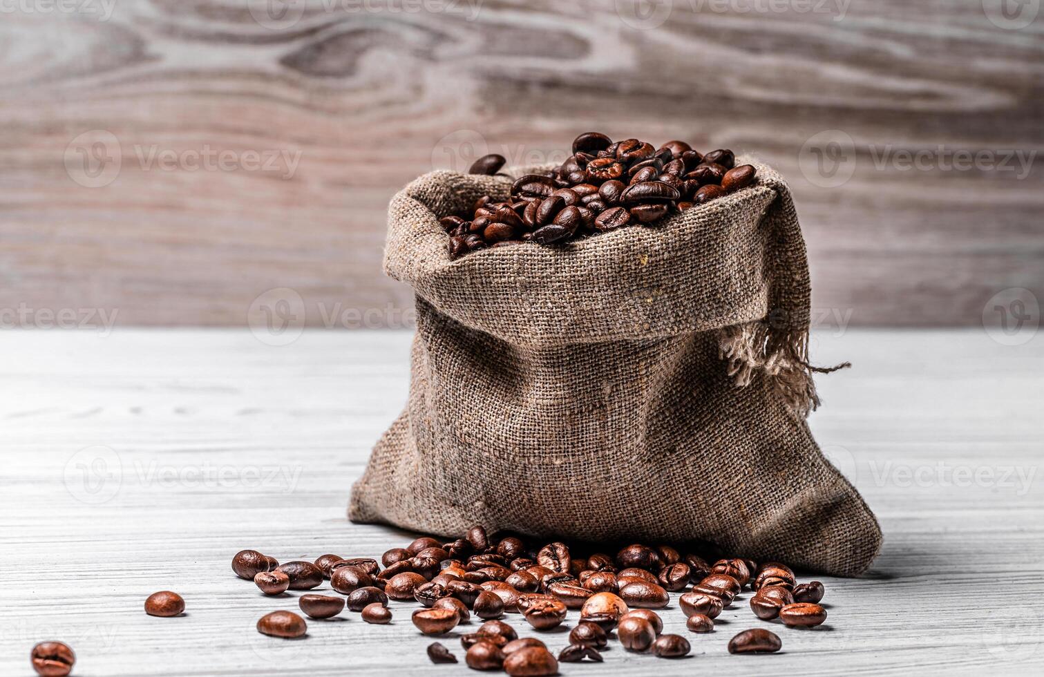 Small burlap bag full of fresh roasted arabica beans and some seeds lying on the table. Sack with brown natural robusta grains on the light surface. photo