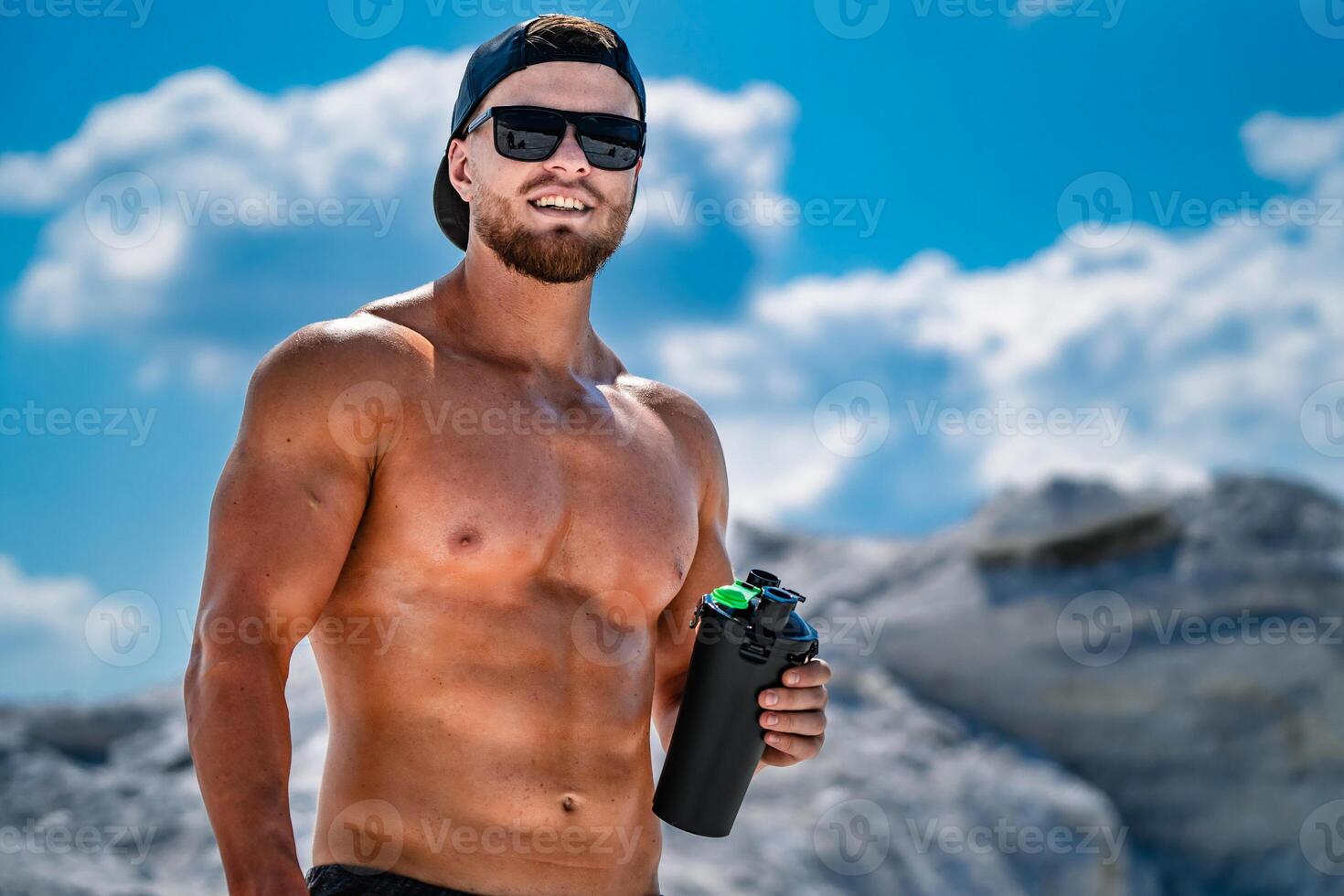 Portrait of a handsome halfnacked bodybuilder man on a mountain with a bottle of water. photo