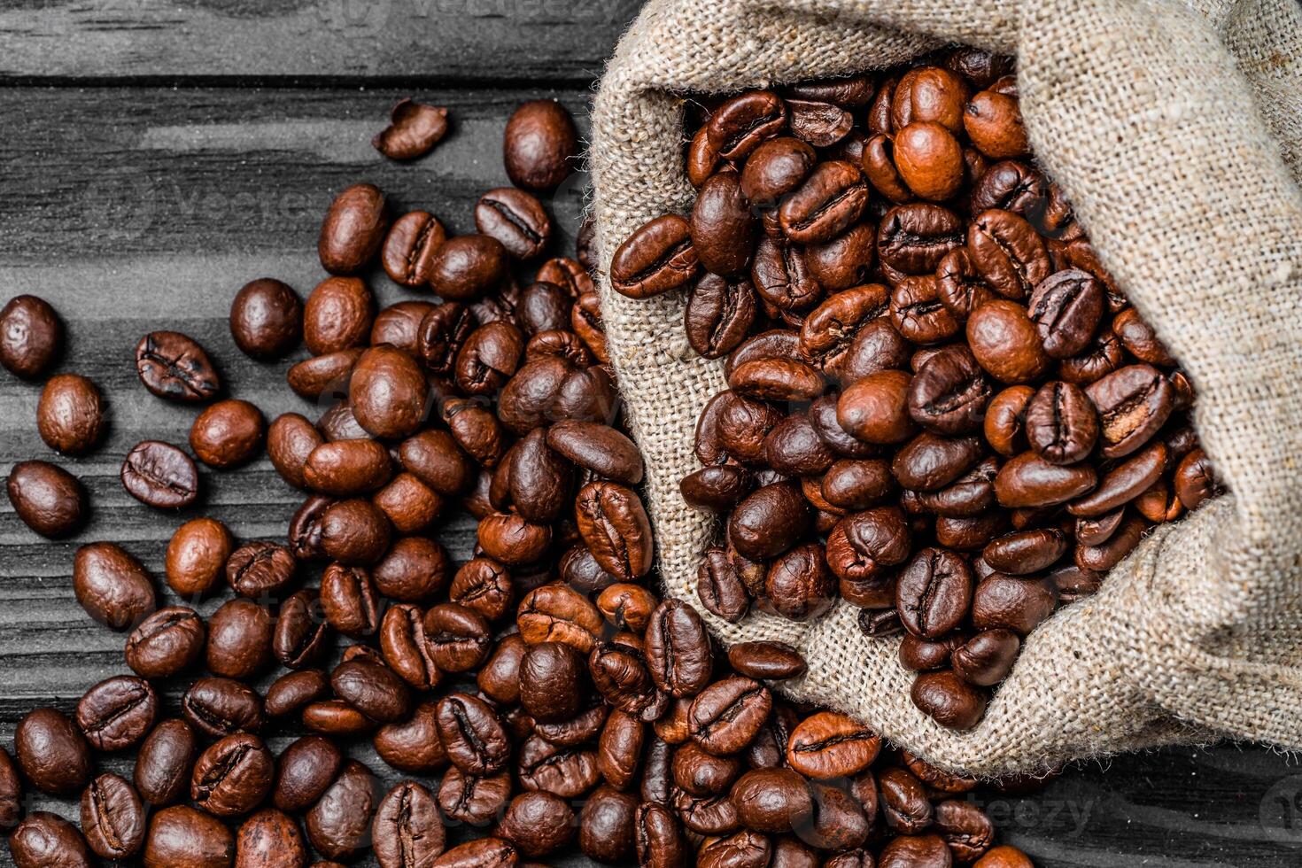 Roasted brown coffee beans falling out from the burlap bag on the table. Fresh natural grains over the gray background. Close-up. photo