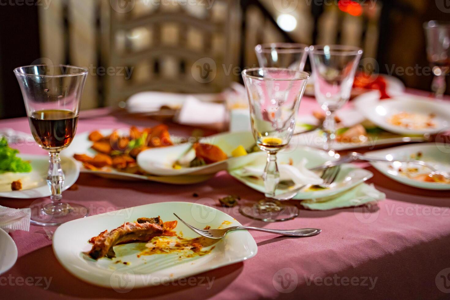 platos con migas de comida y lentes para vino en el mesa con rosado Manteles en el restaurante. permanece de comida en platos después almuerzo o cena. foto