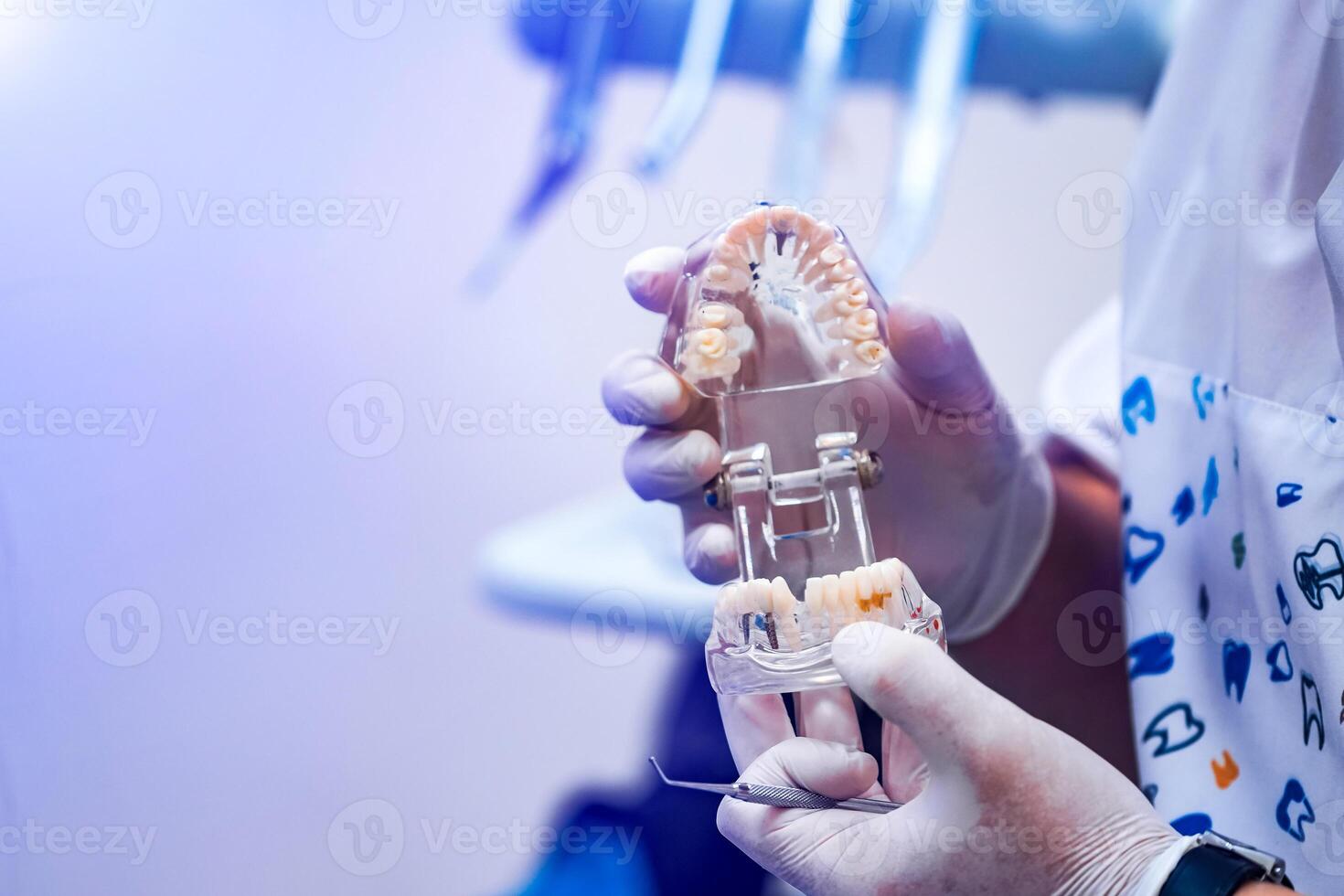 Doctor shows on a plastic jaw sample or model different methods of teeth treatment. Modern dental clinic background. Health concept. White medical gloves on male doctor's hands. photo