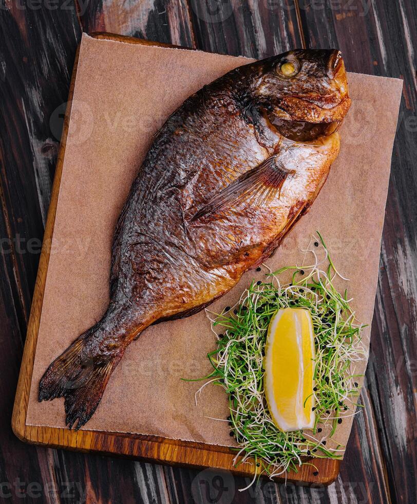 Board with fried dorado on wooden background photo