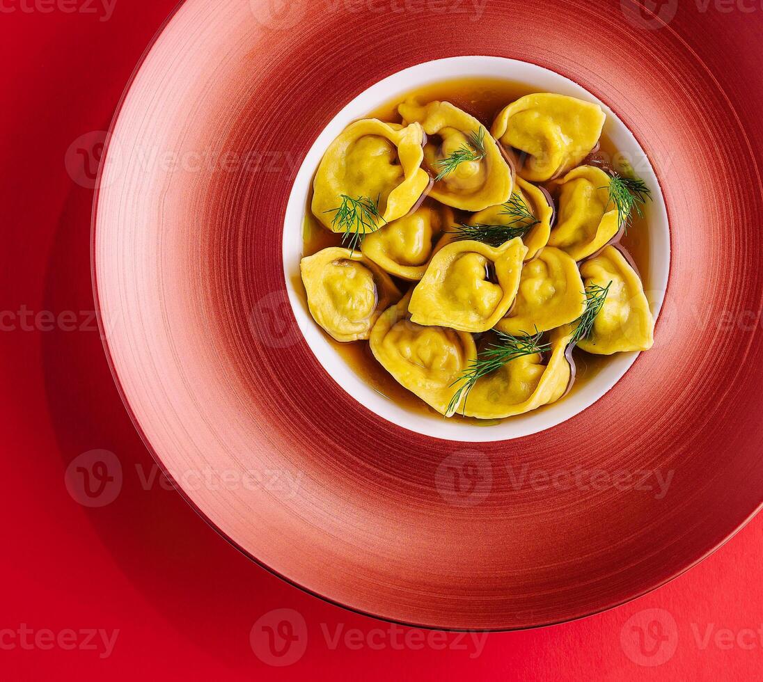 Filled tortellini with herbs on red plate photo